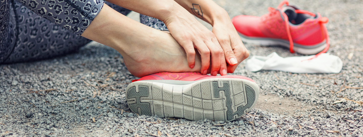 A person sits on the ground, holding onto their foot with both shoes off