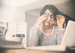 A woman lifts her glasses to rub her eyes