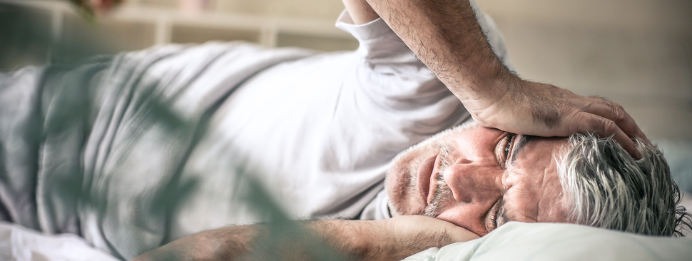 Man lies on bed holding head in pain