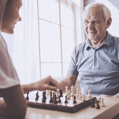 Young woman plays chess with elderly man