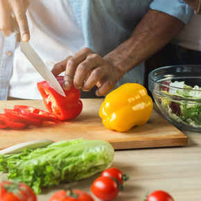 Someone chopping a red pepper with a yellow pepper and lettuce nearby