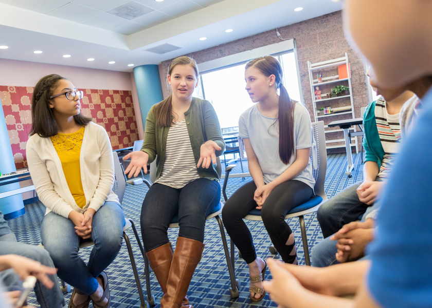 A group of kids sit in a circle as one girl talks animatedly