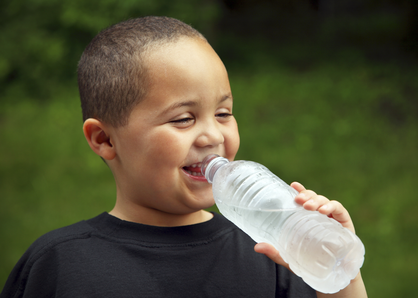 A boy smiles as he drinks from a cold bottle of water