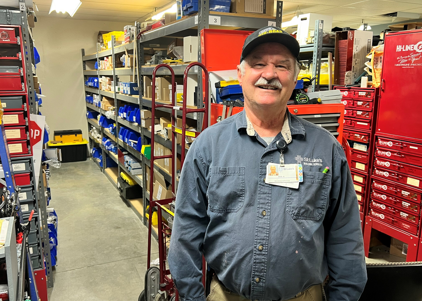 Man wearing grey hat smiles in front of shelving