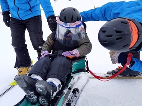 Boy on special sled skis gets ready to go down snowy hill.