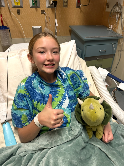 Patient giving a thumbs up from her bed while holding a stuffed animal.