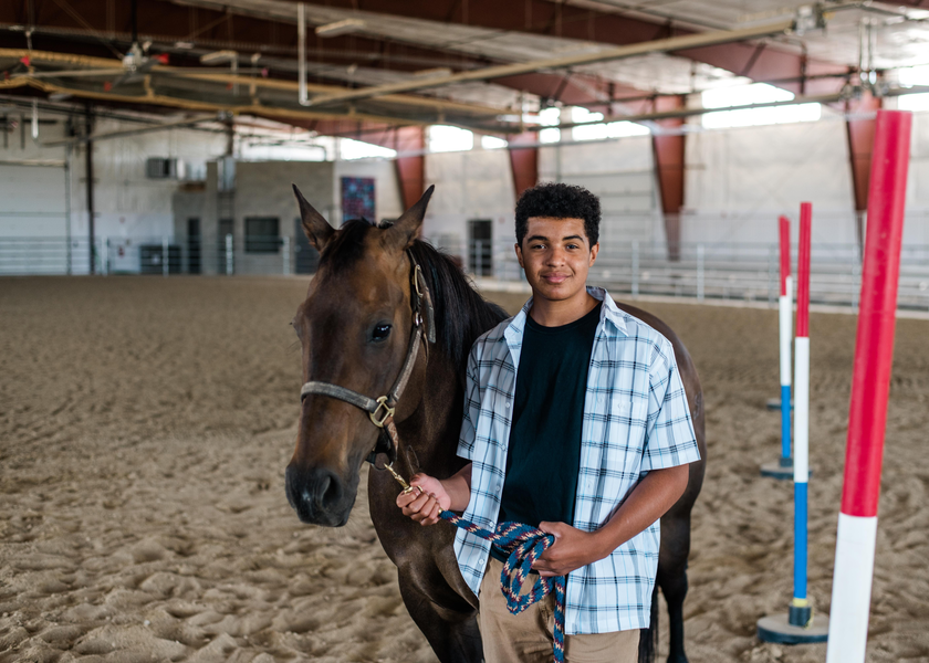 Teen boy holding brown horse's reigns inside arena