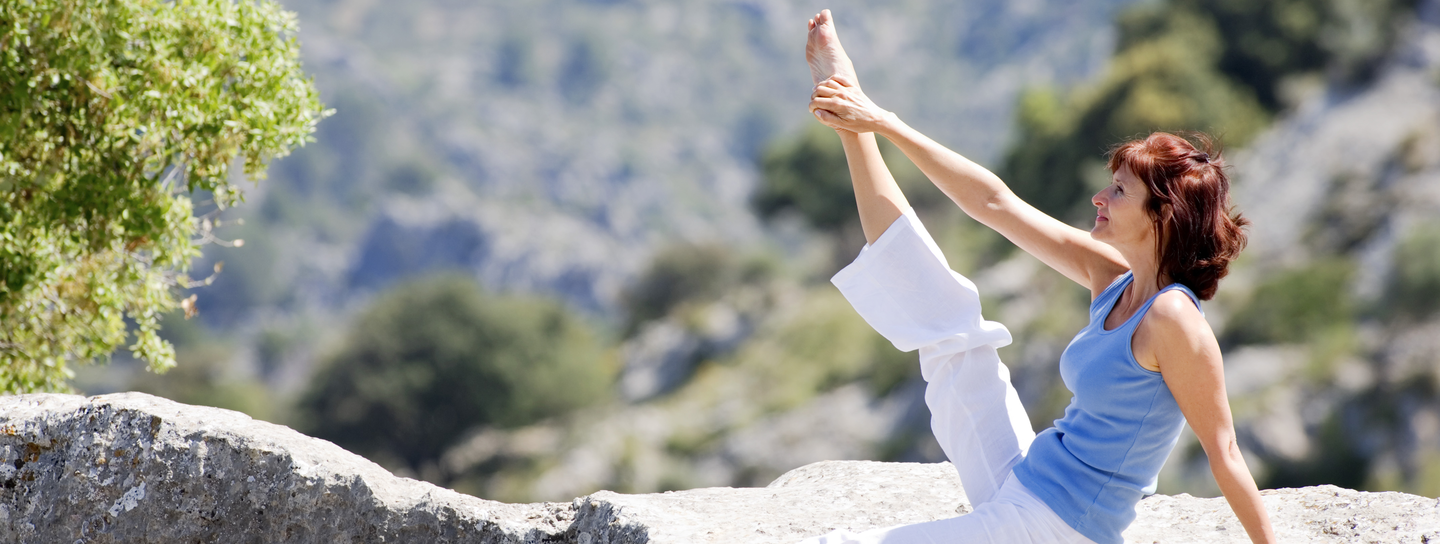 A woman holds a yoga pose while on a mountain outdoors