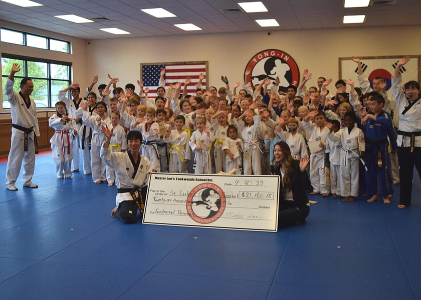  Taekwondo students wave from behind large donation check