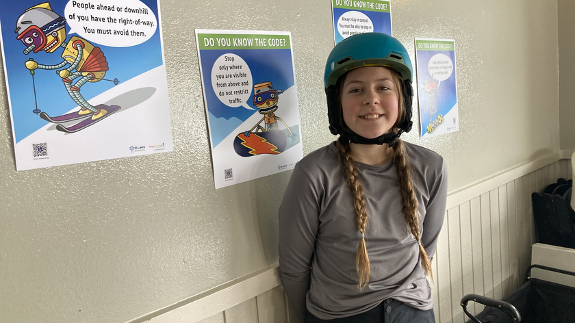  Child wearing a helmet standing in front of ski safety sign.