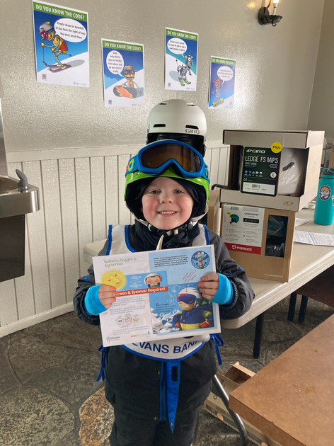   Child wearing a helmet holding winter sports safety sign.