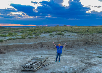 Woman stands in quarry with grassland and sunset in background
