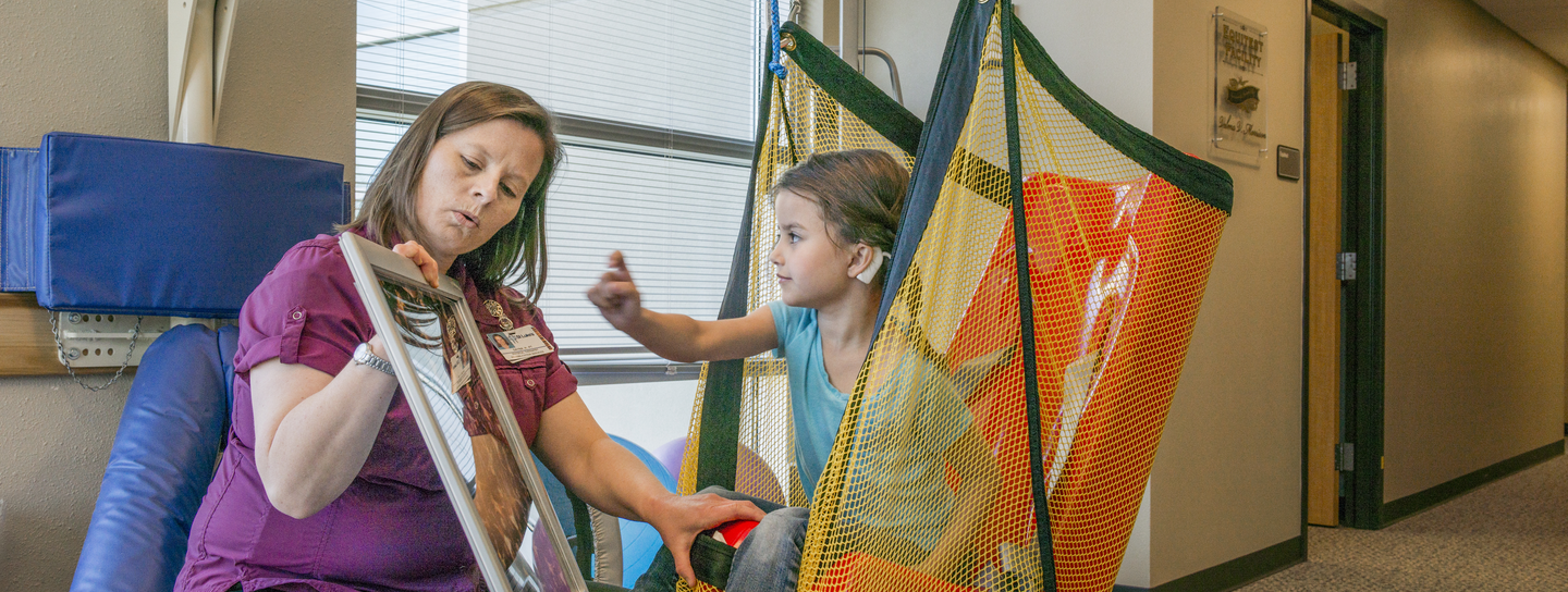 A woman holding a mirror with a girl sitting in a swing.