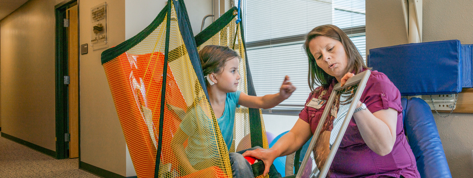 A woman holding a mirror with a girl sitting in a swing.