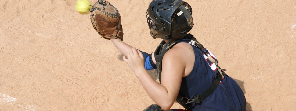 A softball player squats to catch a ball in her mitt