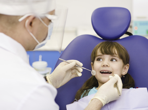 A girl smiles as a doctor checks the her teeth