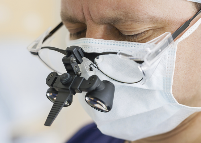A surgeon looks into magnifying glasses while performing surgery