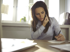 Woman holding a cell phone and writing on paper.