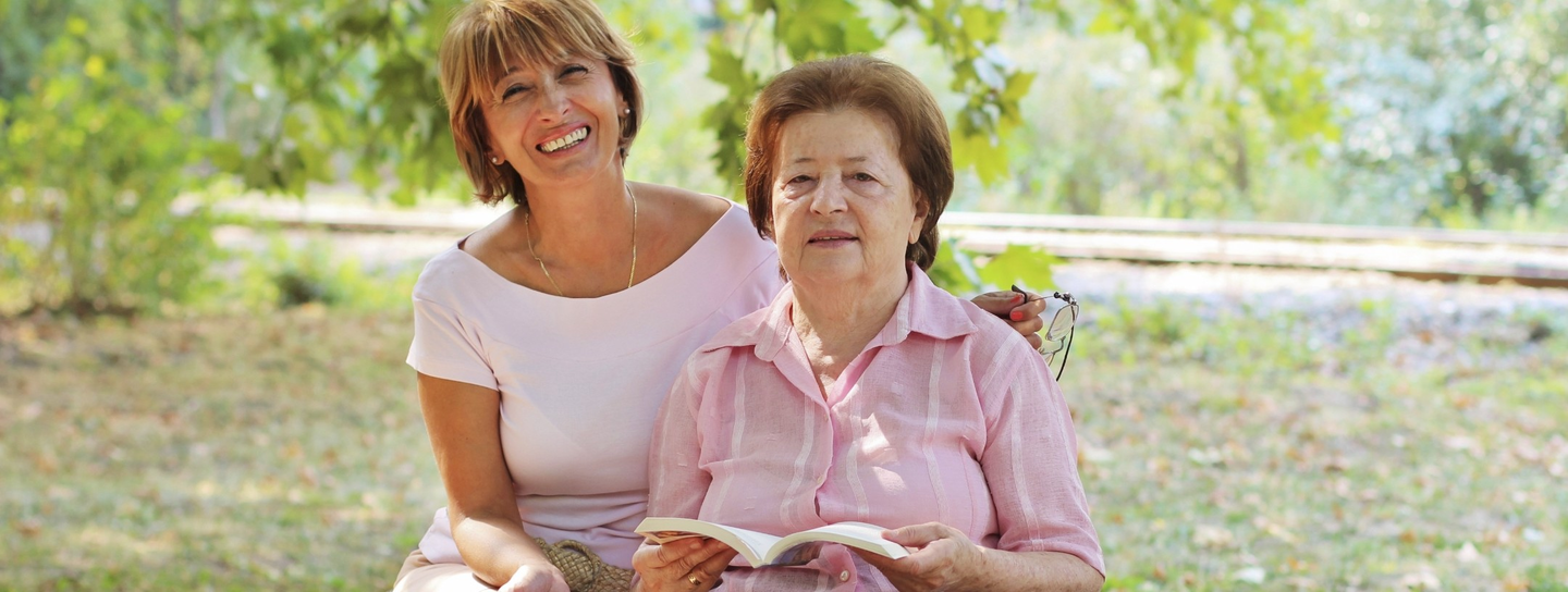 A woman sits on the bench next to her mother, who is holding a book