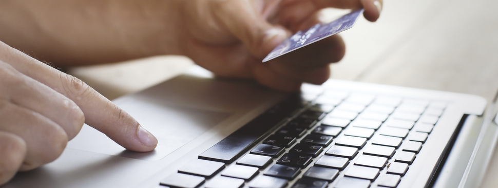 Person holding a credit card in front of a laptop.