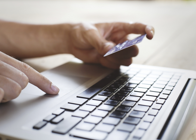 One hand holds a debit card as the other navigates on a computer