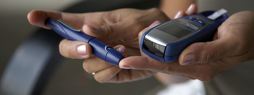 A hand pricks their index finger while holding a monitor