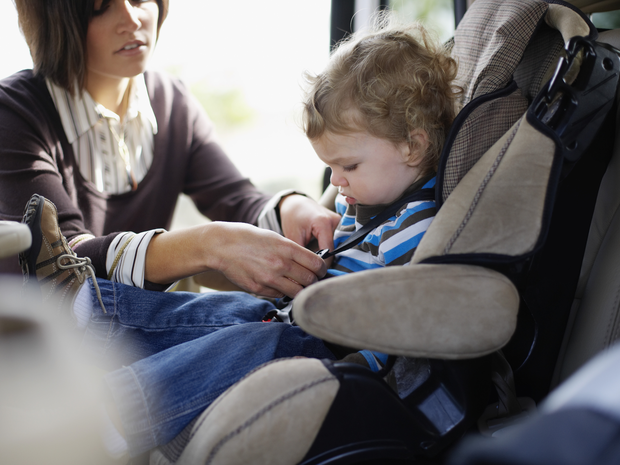 A little boy getting strapped in his carseat.