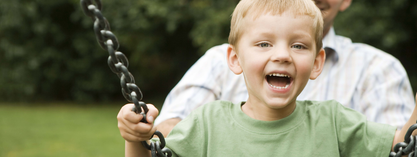 A boy smiles as he swings, being pushed by his father