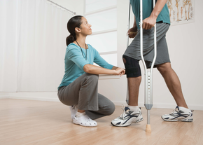 A nurse helps a man in a knee brace use crutches
