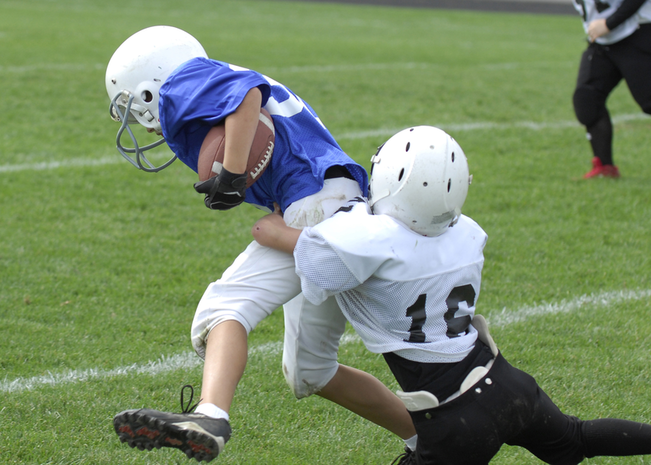 A football player tackles a player on the other team who is holding the ball
