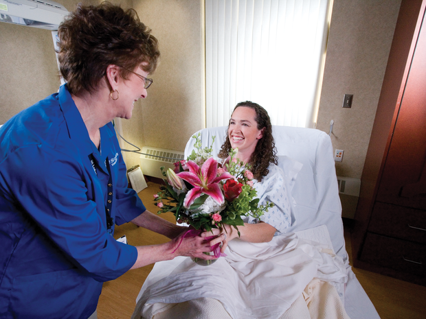Volunteer hands patient flowers while smiling.