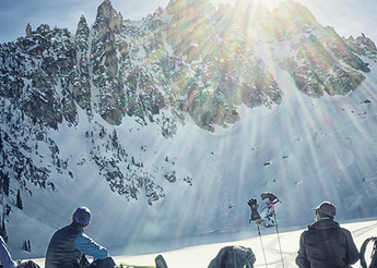 Skiers sitting on a hillside looking at snowy mountain.
