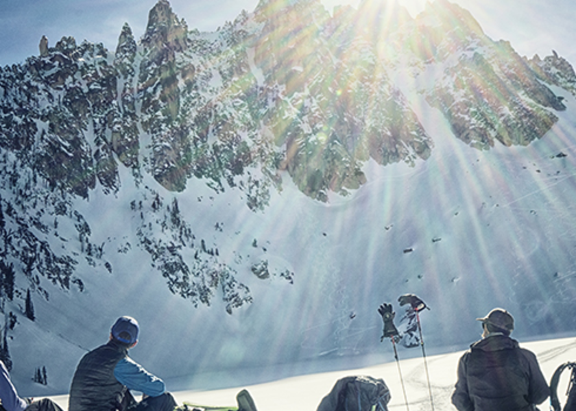 Skiers sitting on a hillside looking at snowy mountain.