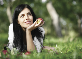 A woman lays in the grass, looking to the sky while holding an apple