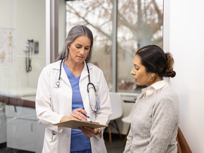 A doctor gestures to her notepad while talking to another professional