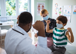 A doctor and child both flex their arm muscles at a checkup
