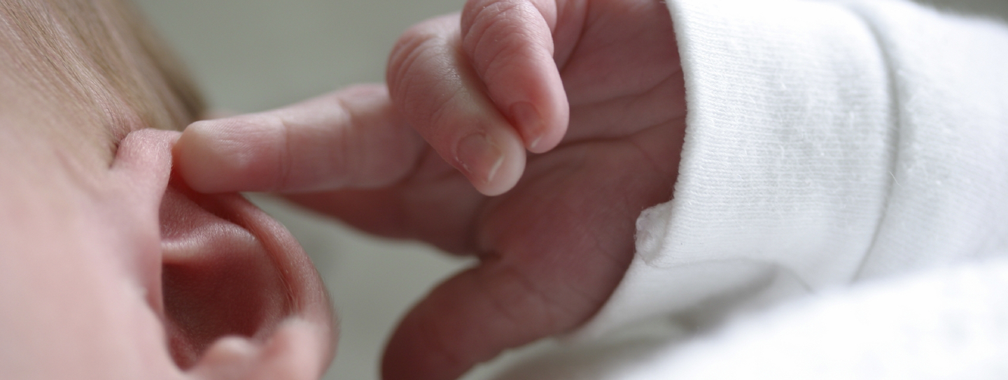 A baby with their finger near their ear