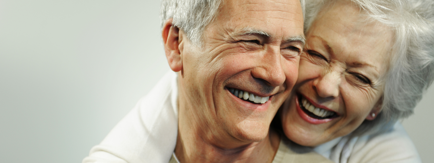 An older woman hugs her husband as both of them smile happily