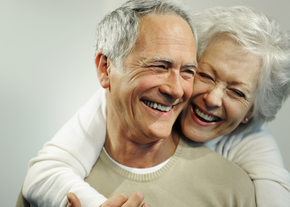 A woman embraces her husband from behind as they both smile
