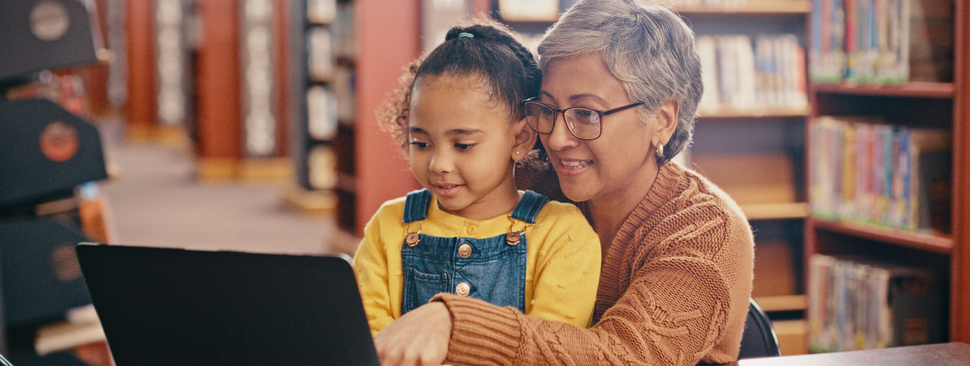 a young girl and her mom look at a laptop in the library