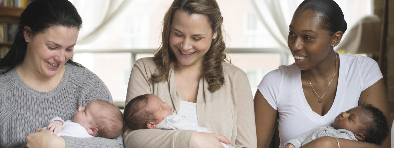 Moms holding their babies on a sofa.