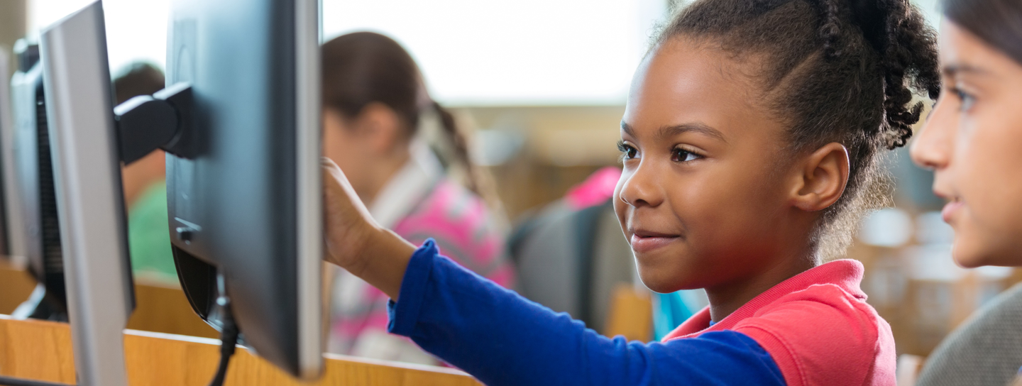A young girl gestures at a computer screen in front of her