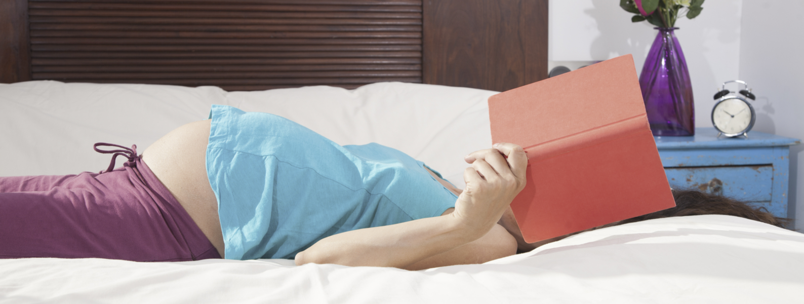 Pregnant woman lying in bed reading.