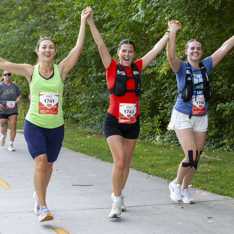 Three friends holding hands as they run the FitOne half marathon together