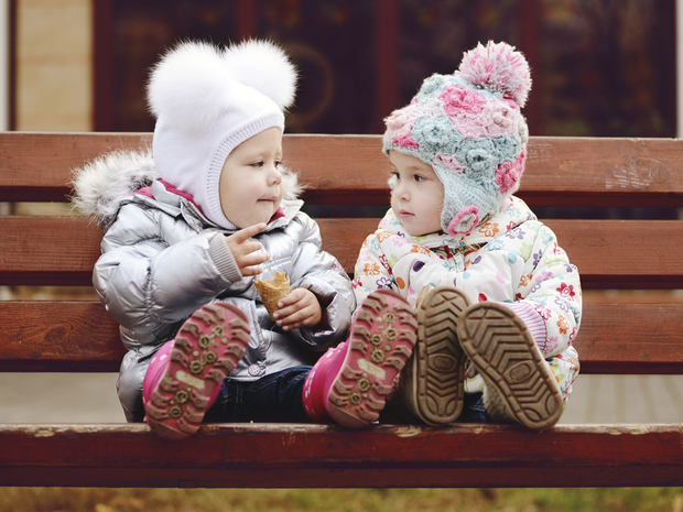 Two babies in coats sit on a bench