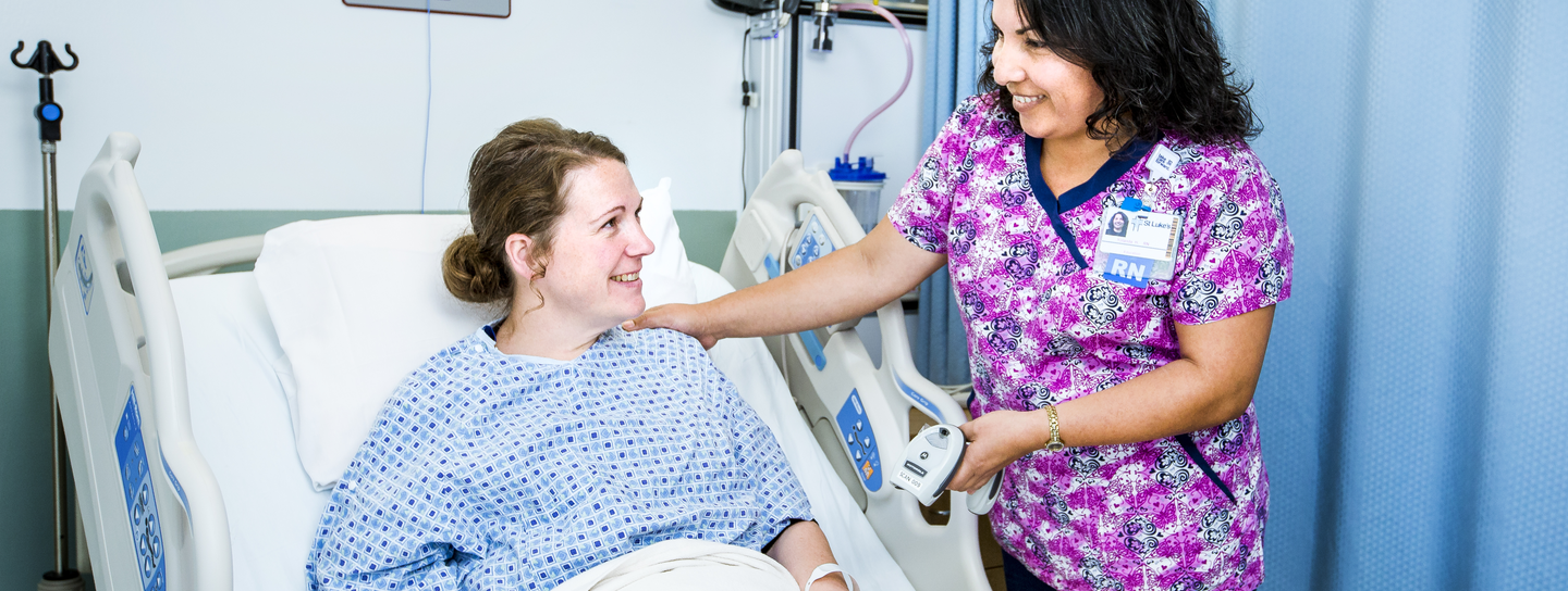 Provider smiles while tending to patient in hospital bed.