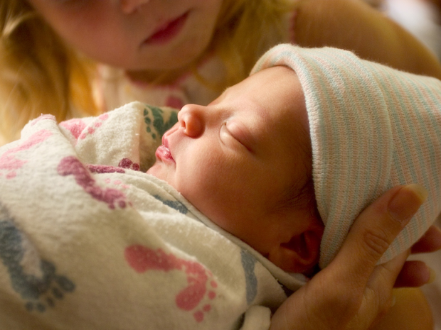 Newborn sleeping as big sister watches.