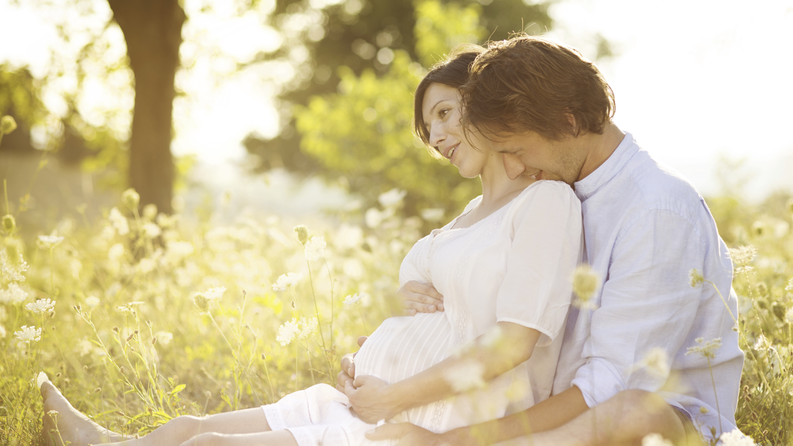 A pregnant couple sitting in a summer field.