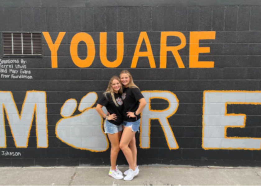 Two young women stand in front of mural
